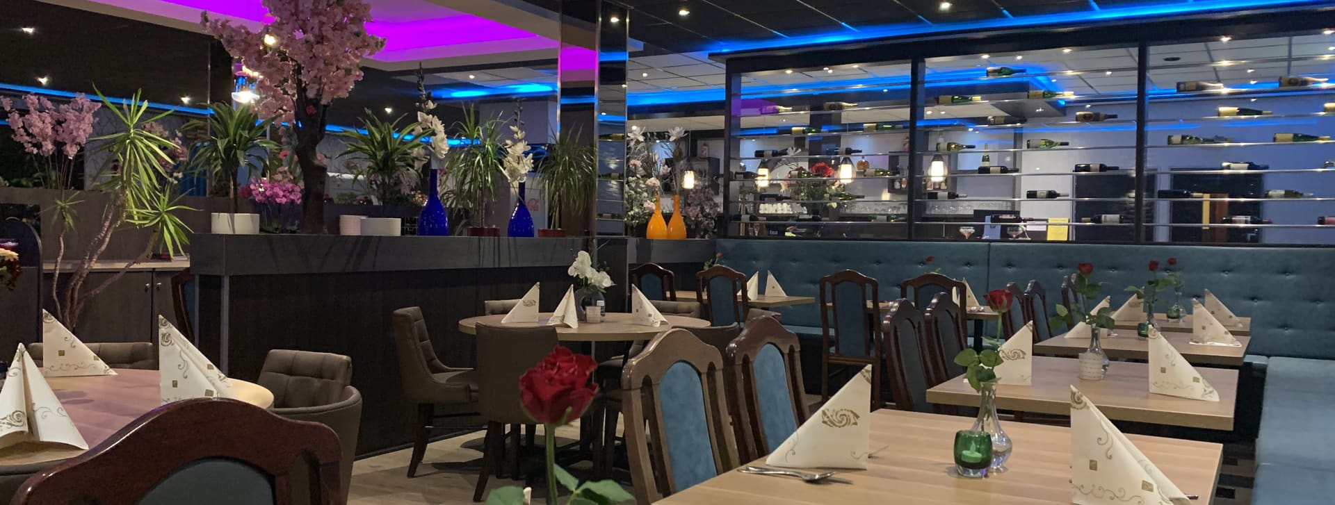 De eetzaal van Sozing bij avond, met gedekte tafels, kersenbloesem en blauwe sfeerverlichting langs het plafond.