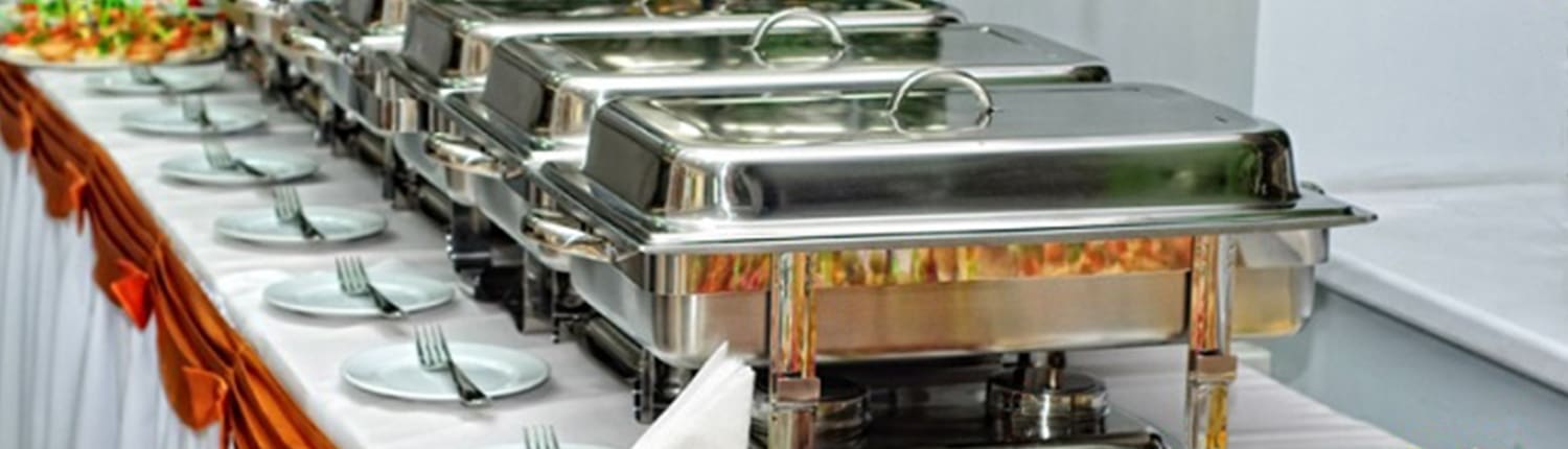 Een buffettafel met chafing dishes, borden en bestek klaargezet voor een feest.