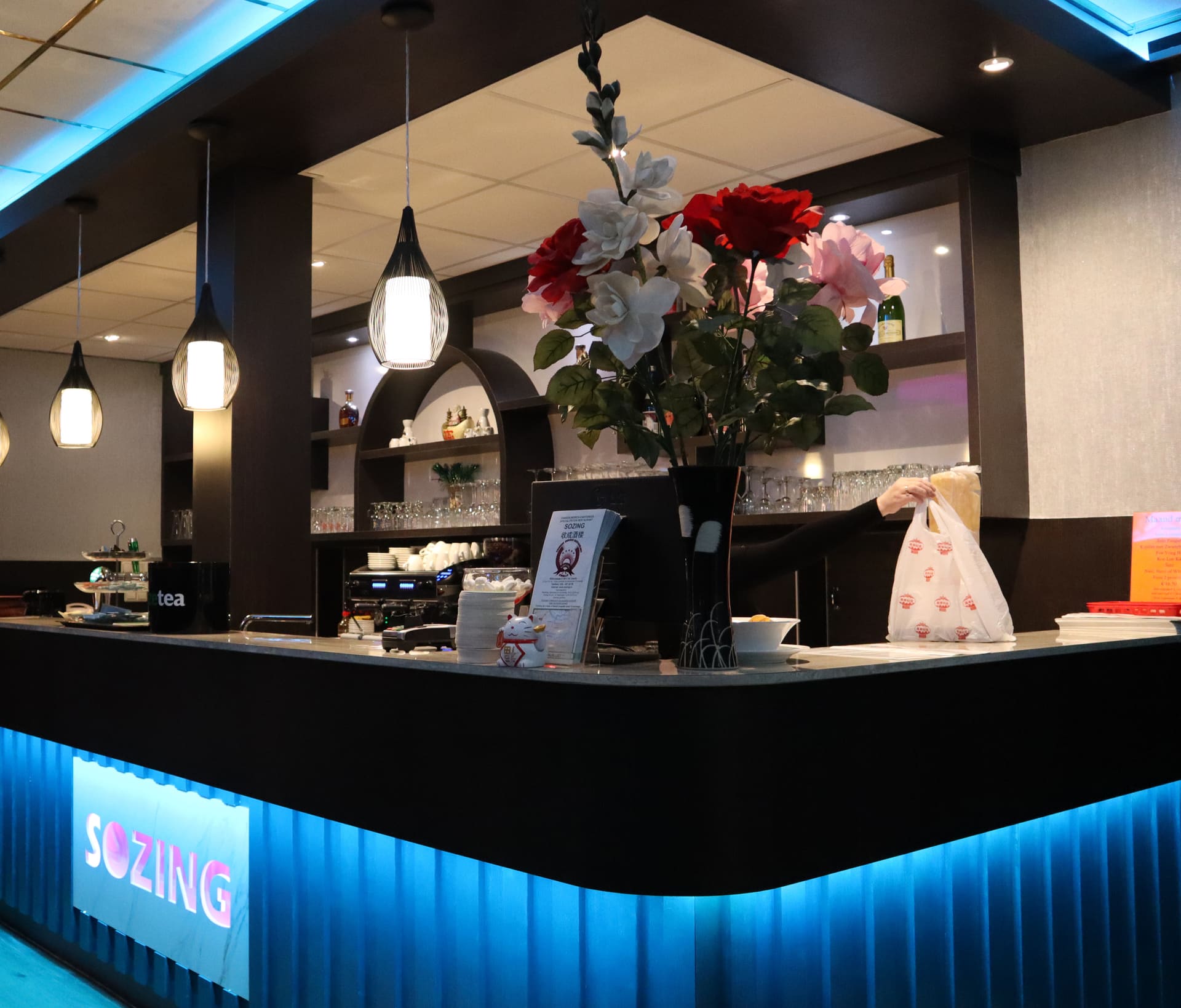 De bar van Sozing met het verlichte SOZING-bord, hangende lampen en een boeket zijden rozen.